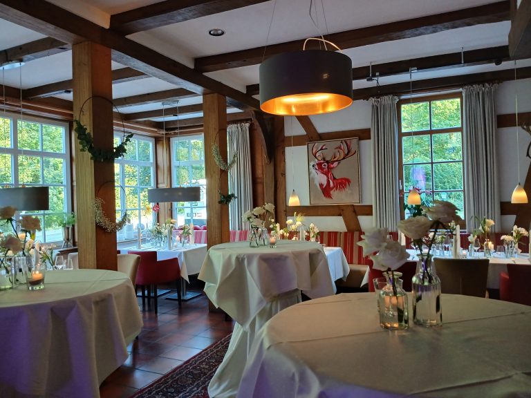 Ein gemütliches Restaurant mit Holzdekor, eleganten Tischen, Blumenarrangements und einem Gemälde eines Rehs an der Wand.