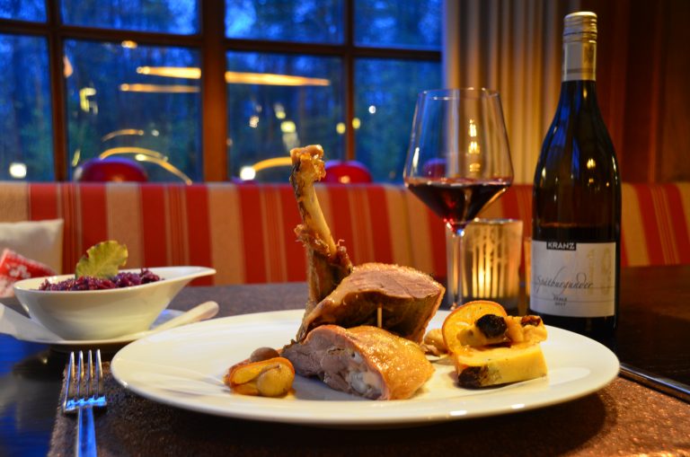 Ein Teller mit zartem Fleisch, gebratenen Kartoffeln und Rotkohl, begleitet von einem Glas Rotwein und einer Kerze.